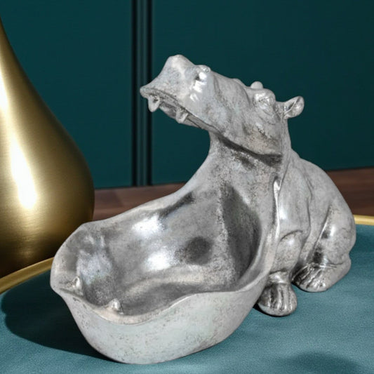 Silver hippo figurine on a teal surface with a gold vase in the background
