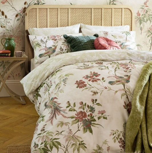 Floral bedding set on a bed with matching headboard and side table in a room with floral wallpaper.