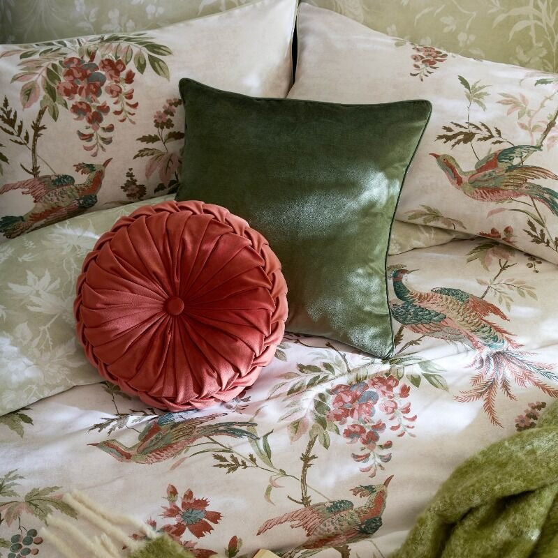 Cushions on a floral bedspread with decorative pillows and a green blanket.
