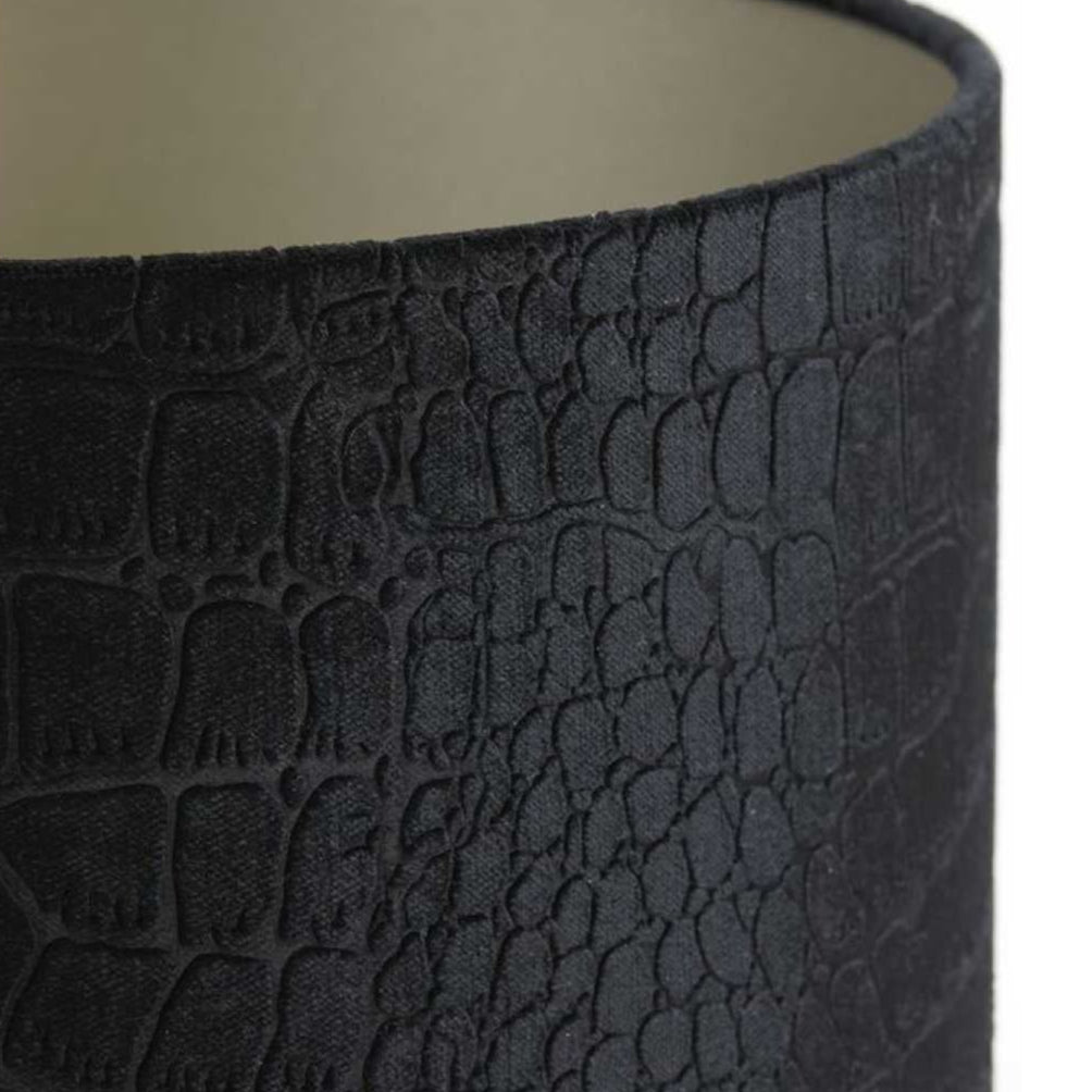 A cylindrical black lampshade with a textured, faux crocodile skin pattern and a light-coloured interior.