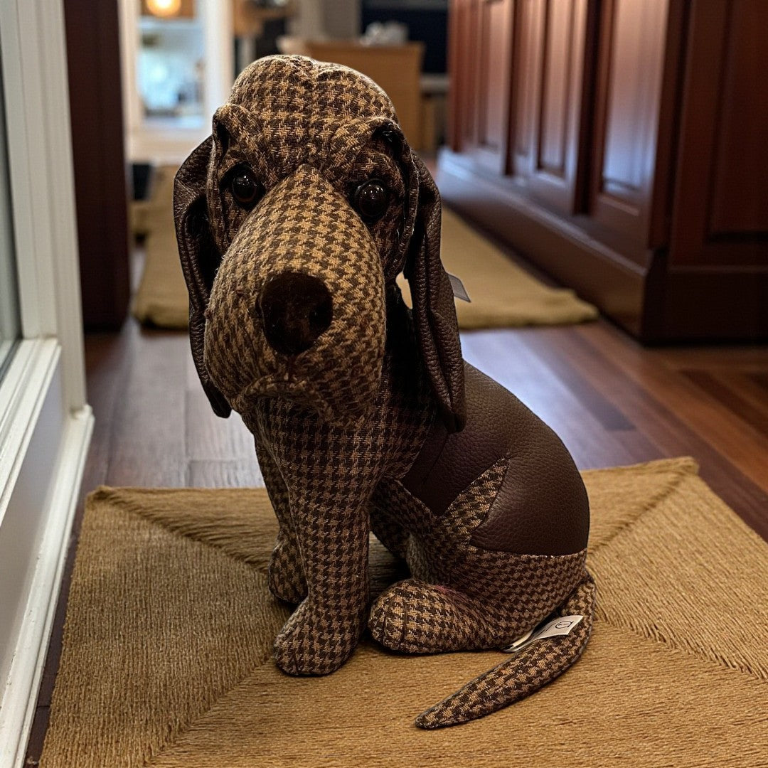 Stuffed dog toy with houndstooth pattern on a doormat inside a house.