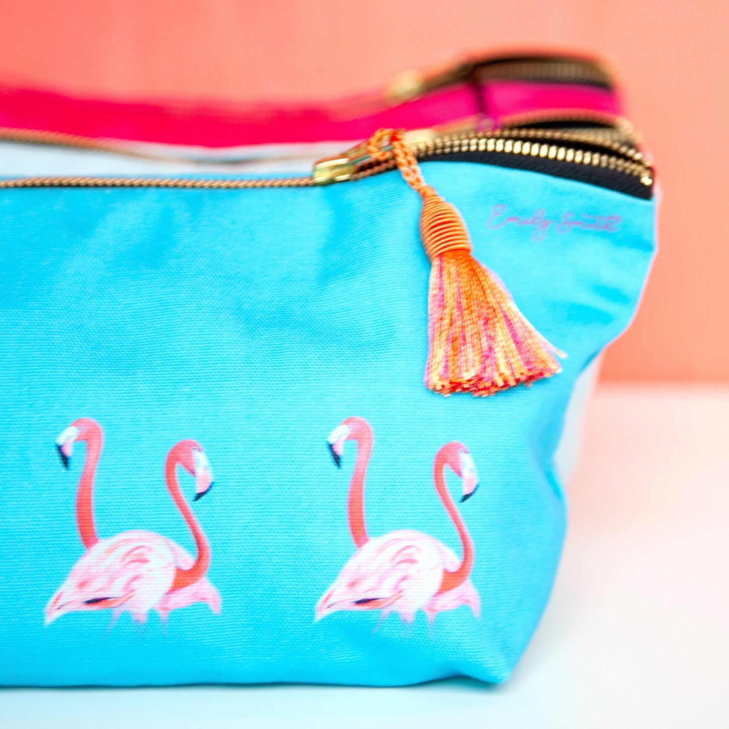 Blue pouch with pink flamingo design and tassel on a peach background