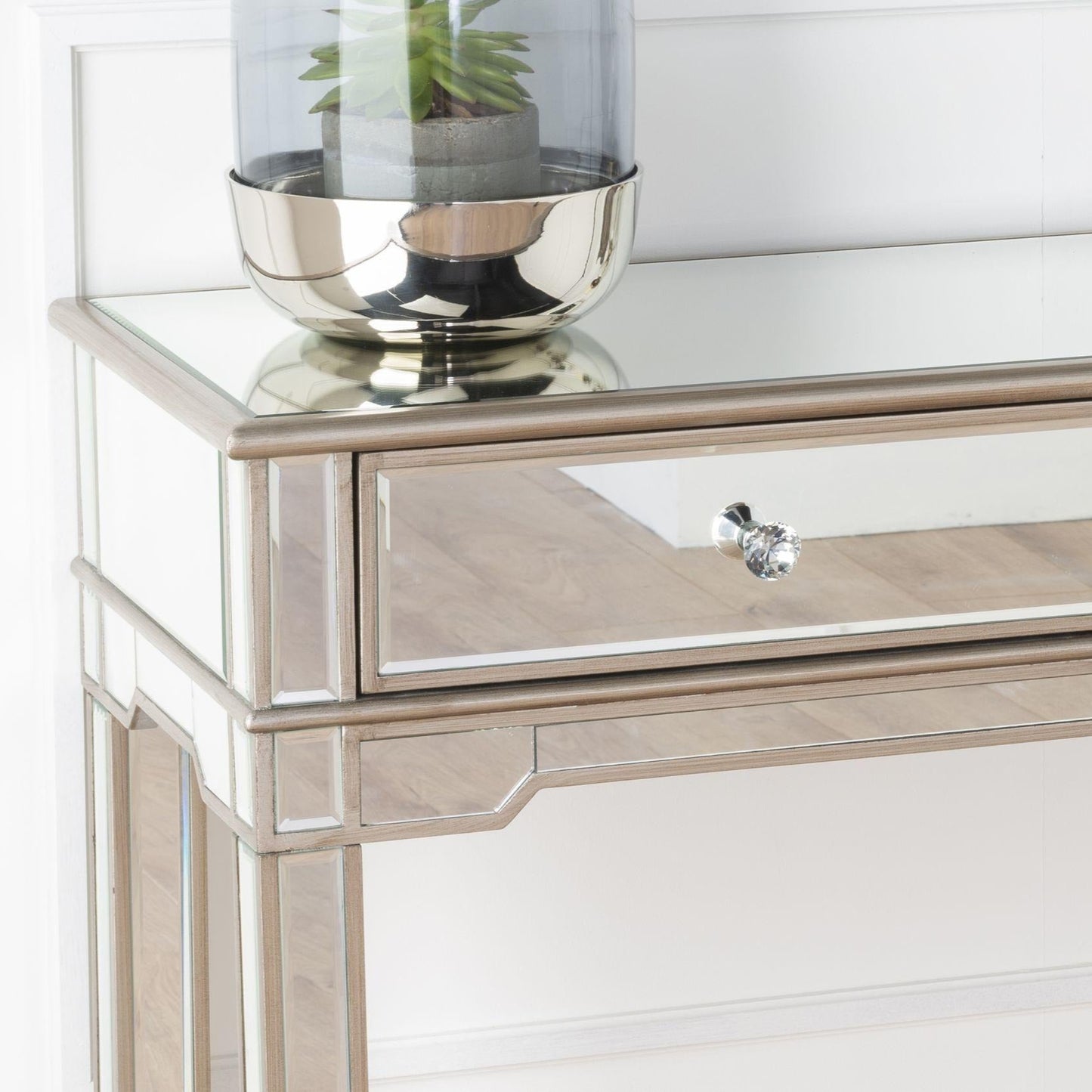 Decorative console table with mirrored surface and glass bowl on a white background