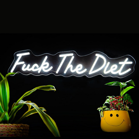 Neon sign with 'Fuck The Diet' text between two potted plants on a black background