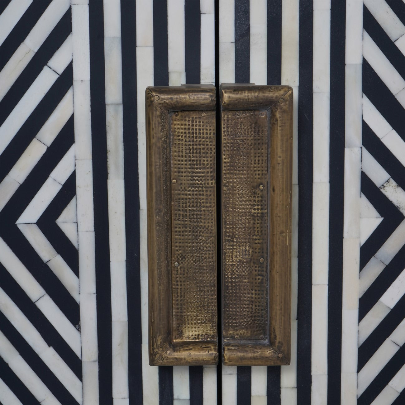 Pair of bronze door handles on a black and white geometric patterned cabinet.