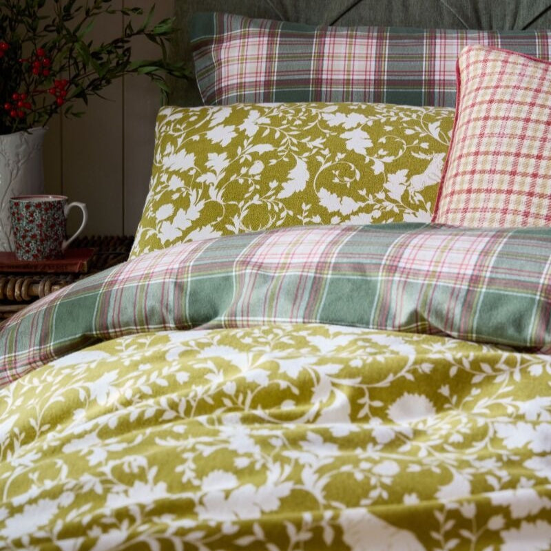 Plaid and floral patterned bedding on a bed with a wooden headboard.