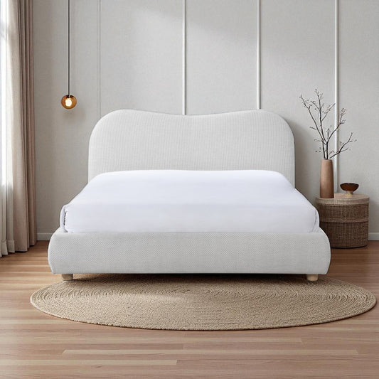 White upholstered bed in a minimalistic room with wooden flooring and a small table.