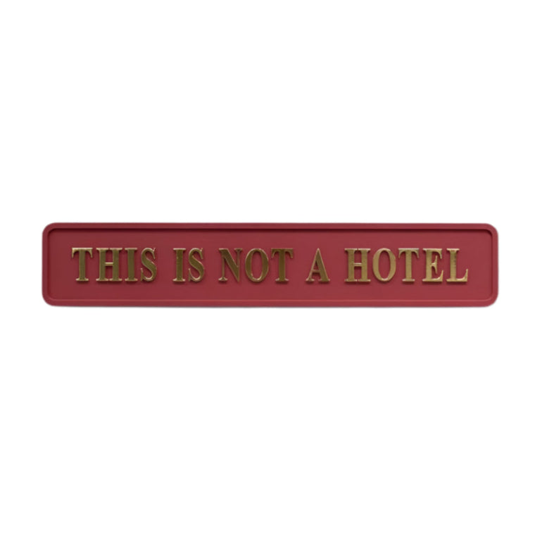 A red and gold sign with 3D gold foil lettering that reads 'THIS IS NOT A HOTEL'.