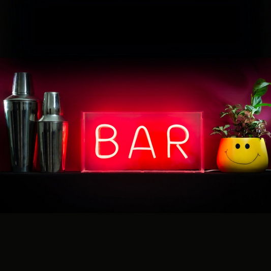 Neon 'BAR' sign with cocktail shakers and a plant on a dark background