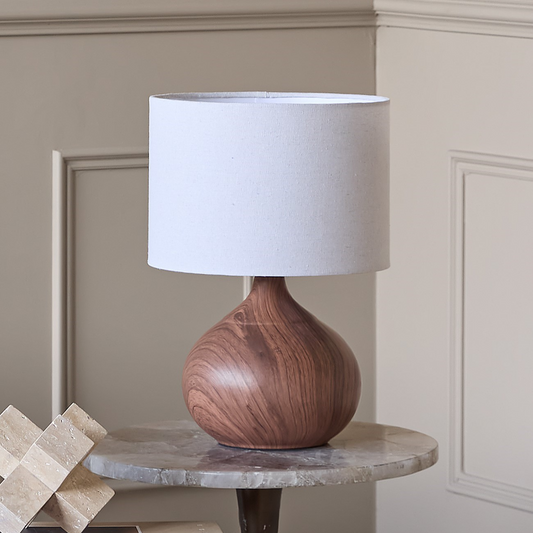 Wooden table lamp with a white shade on a marble surface against a neutral wall.