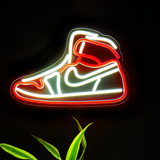 Neon shoe sign above a potted plant on a black background