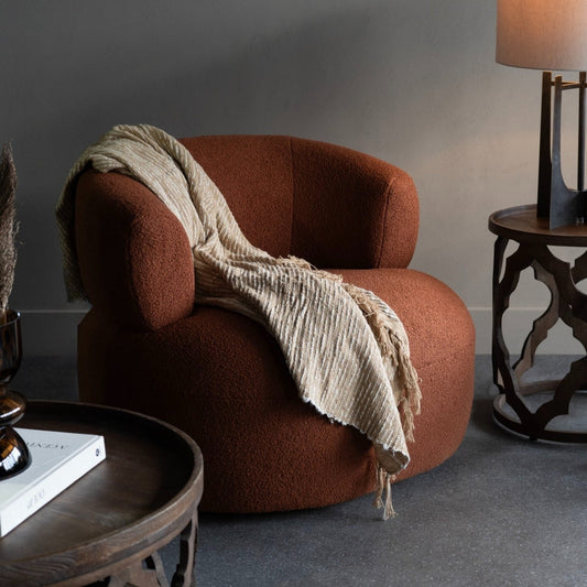 terracotta armchair with a beige blanket in a room with a grey wall and wooden side table.