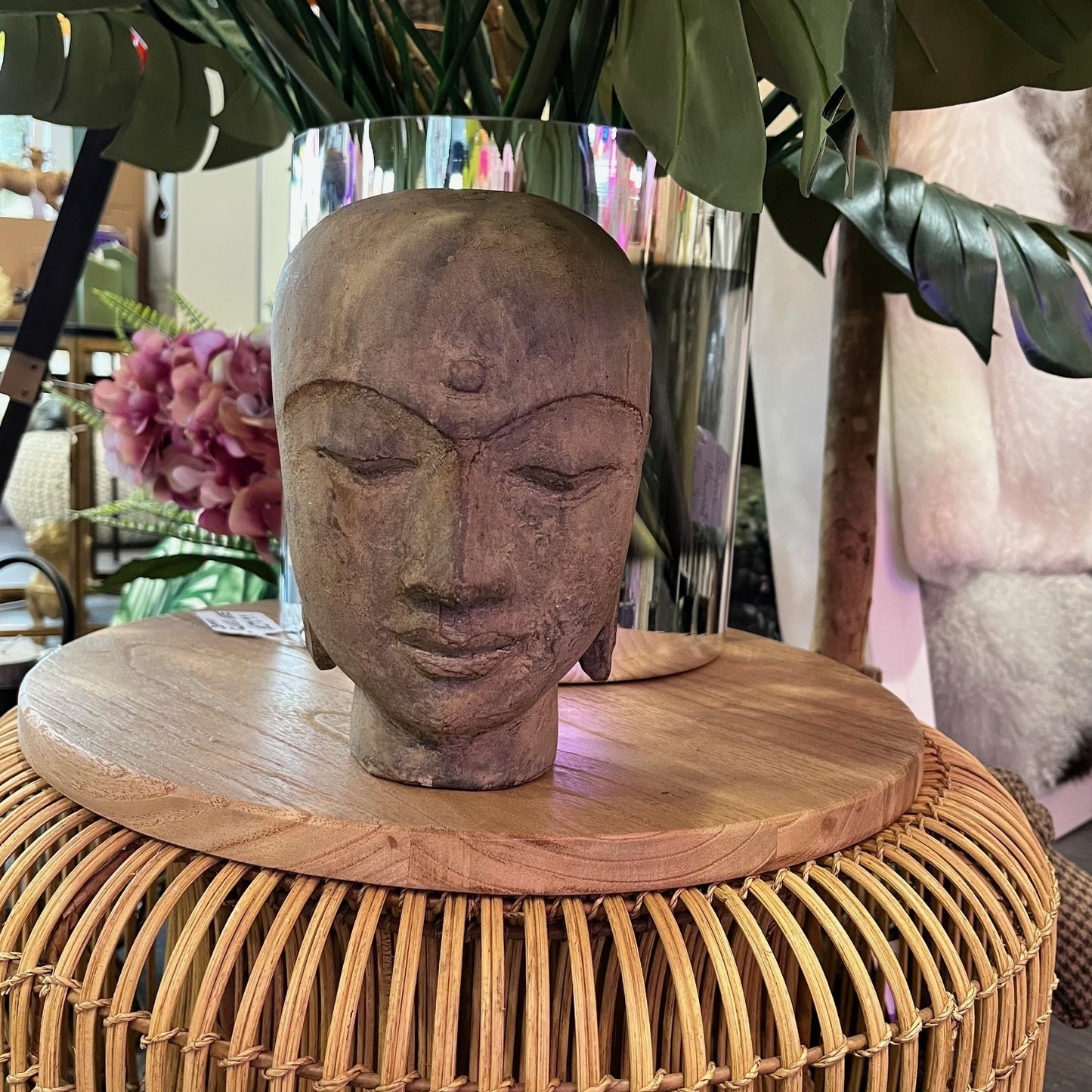 A table showing a grey Stone Monk Head, a monk with its eyes closed in peaceful meditation, reminiscent of Buddha. Surrounded by flowers.