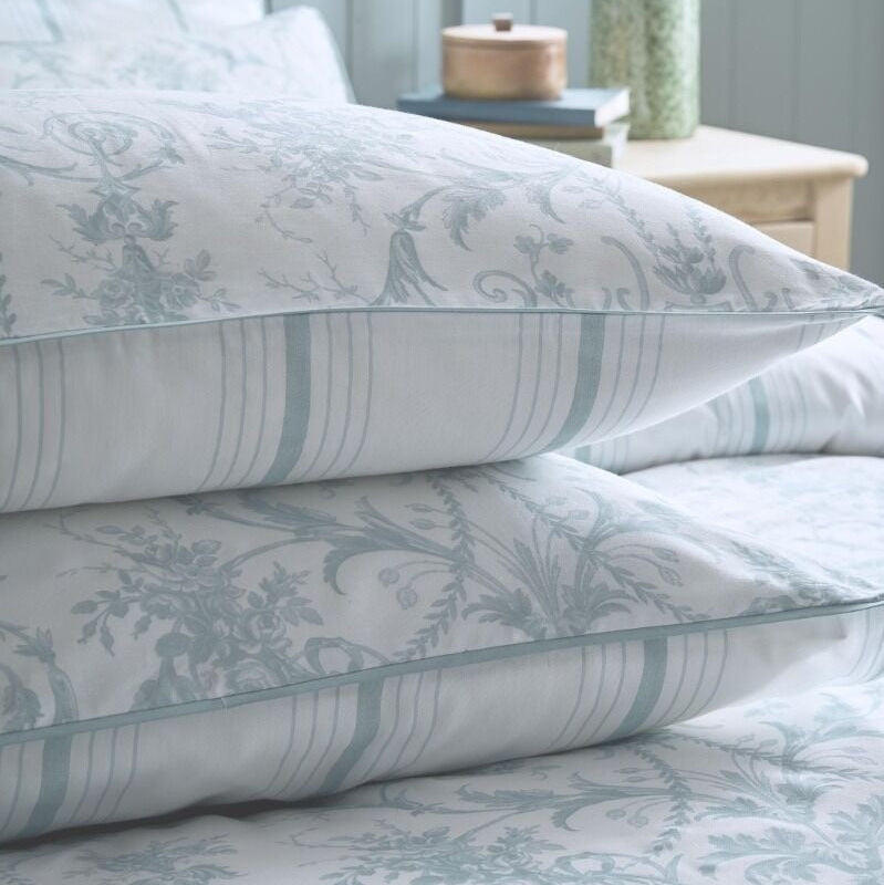 Stack of patterned pillows on a bed with a light blue wall and plant in the background