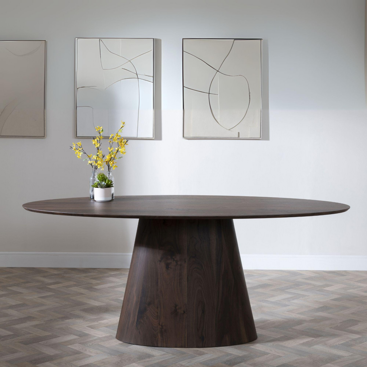 Wooden dining table with a vase of yellow flowers in a room with abstract art on the wall.