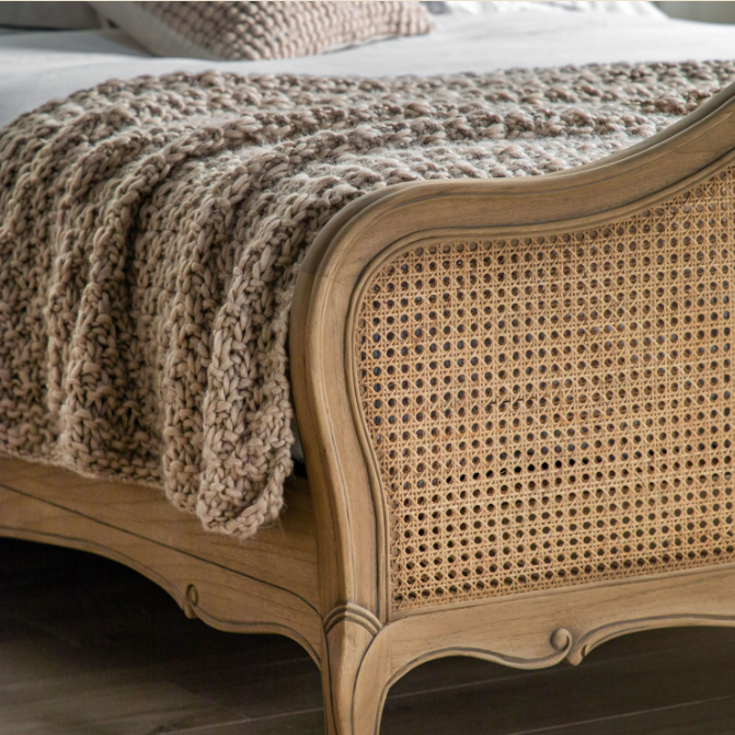Wooden bed with wicker headboard and textured beige blanket