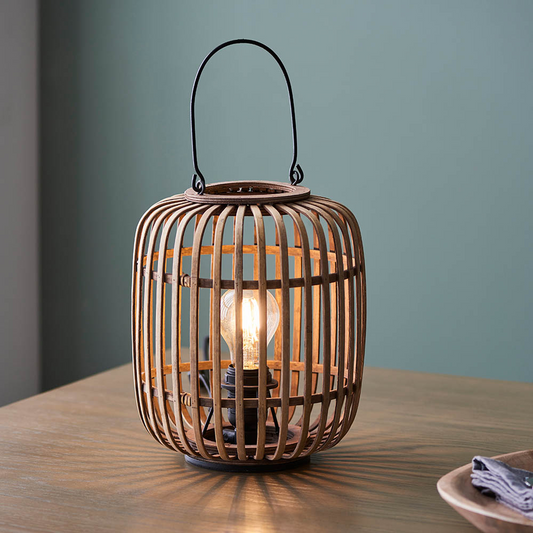 Wooden lantern with a light bulb inside on a wooden table against a teal wall.