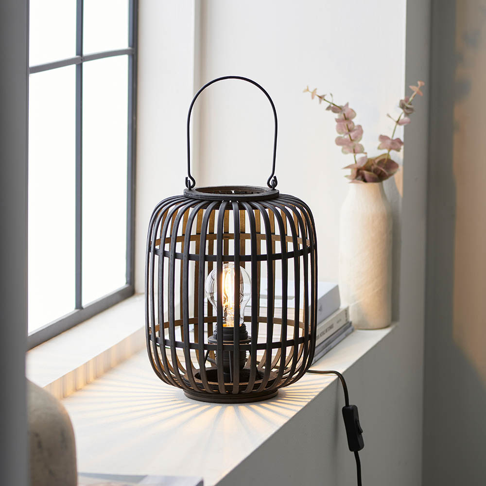 Black woven table lamp on a windowsill with a vase of flowers in the background
