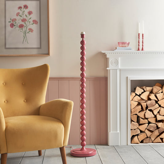 Pink lamp base in a living room with a yellow armchair and fireplace.