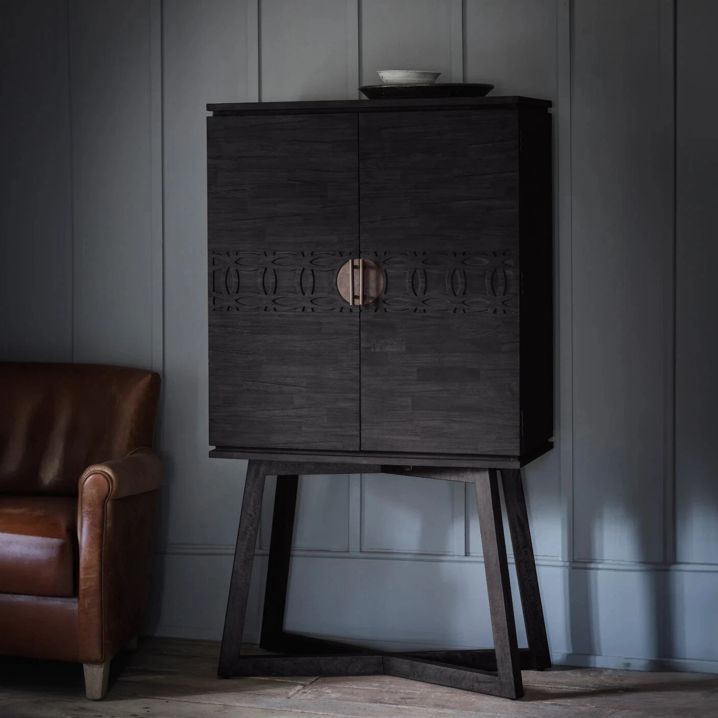Dark wooden cabinet with decorative elements against a gray wall, next to a brown leather armchair.