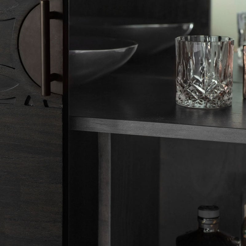 Close-up of a dark wooden shelf with a glass container and a bottle.