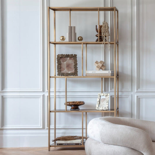 Gold metal shelf with decorative items against a white paneled wall