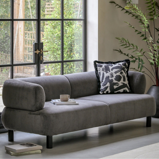 Gray sofa with a decorative pillow in a room with large windows and a plant.