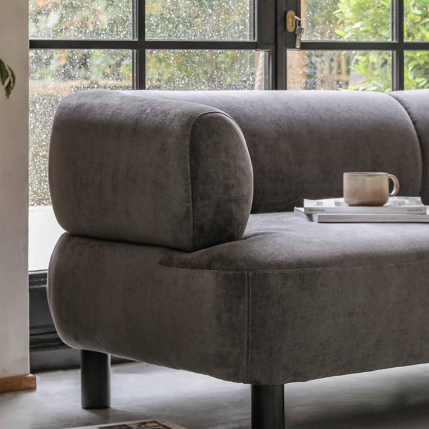 Gray sofa with a cup and book in a room with large windows.