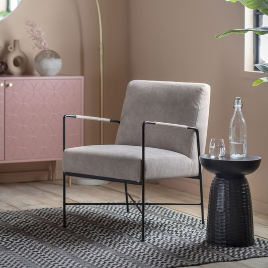 Modern living room with a gray armchair, black side table, and pink cabinet.