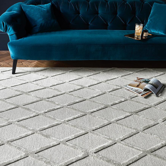 Blue velvet sofa with a coffee table and drinks on a patterned rug in a room.