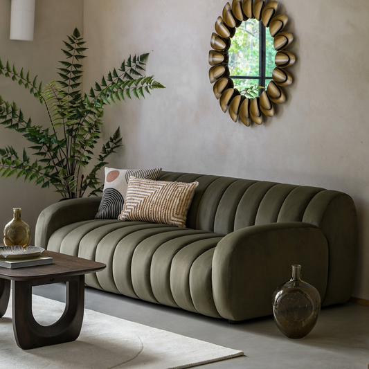 Modern living room with a green sofa, decorative mirror, and plants.