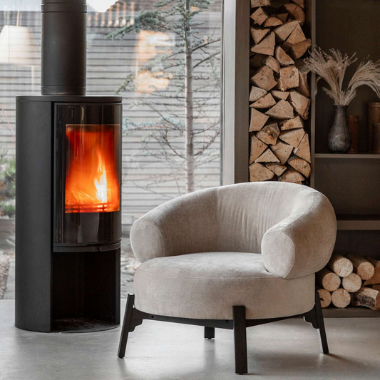 Modern armchair in a room with a lit stove and stacked firewood.