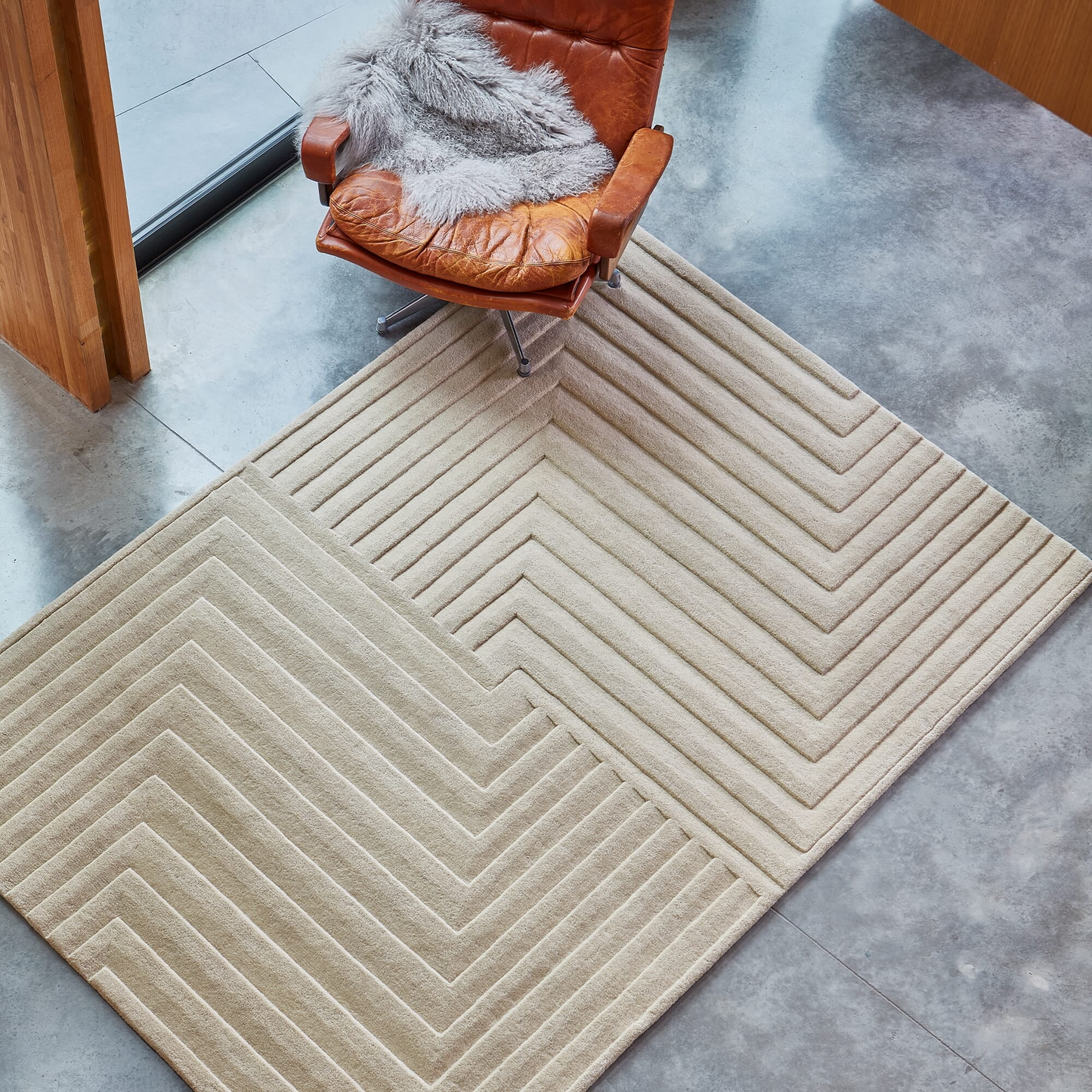 Beige area rug with geometric pattern on a gray floor, featuring a brown chair with a fur cover.