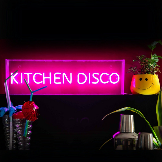 Neon sign reading 'KITCHEN DISCO' in a dark setting with decorative items.
