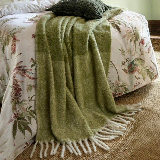 Green blanket with fringes draped over a floral-patterned bed