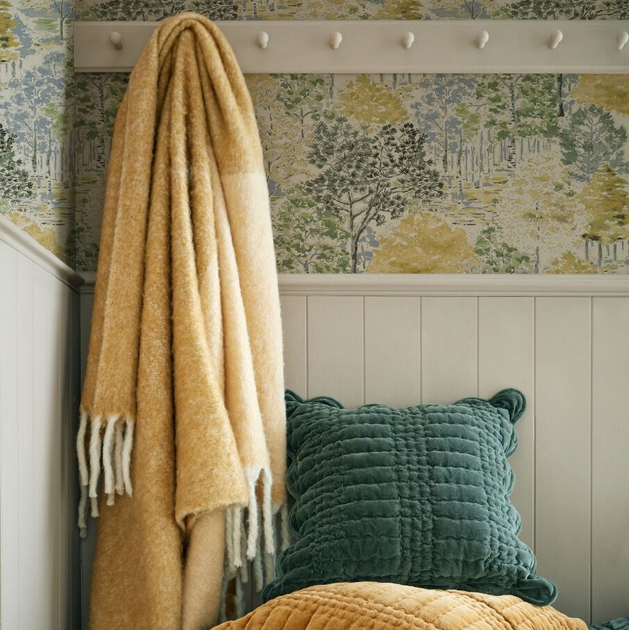 Yellow blanket draped over a chair with green cushions against a floral wallpapered wall.