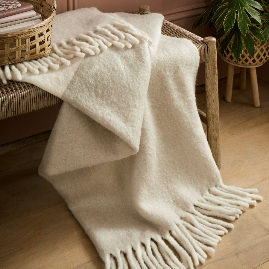beige blanket with fringe draped over a wicker chair in a warm-toned room.