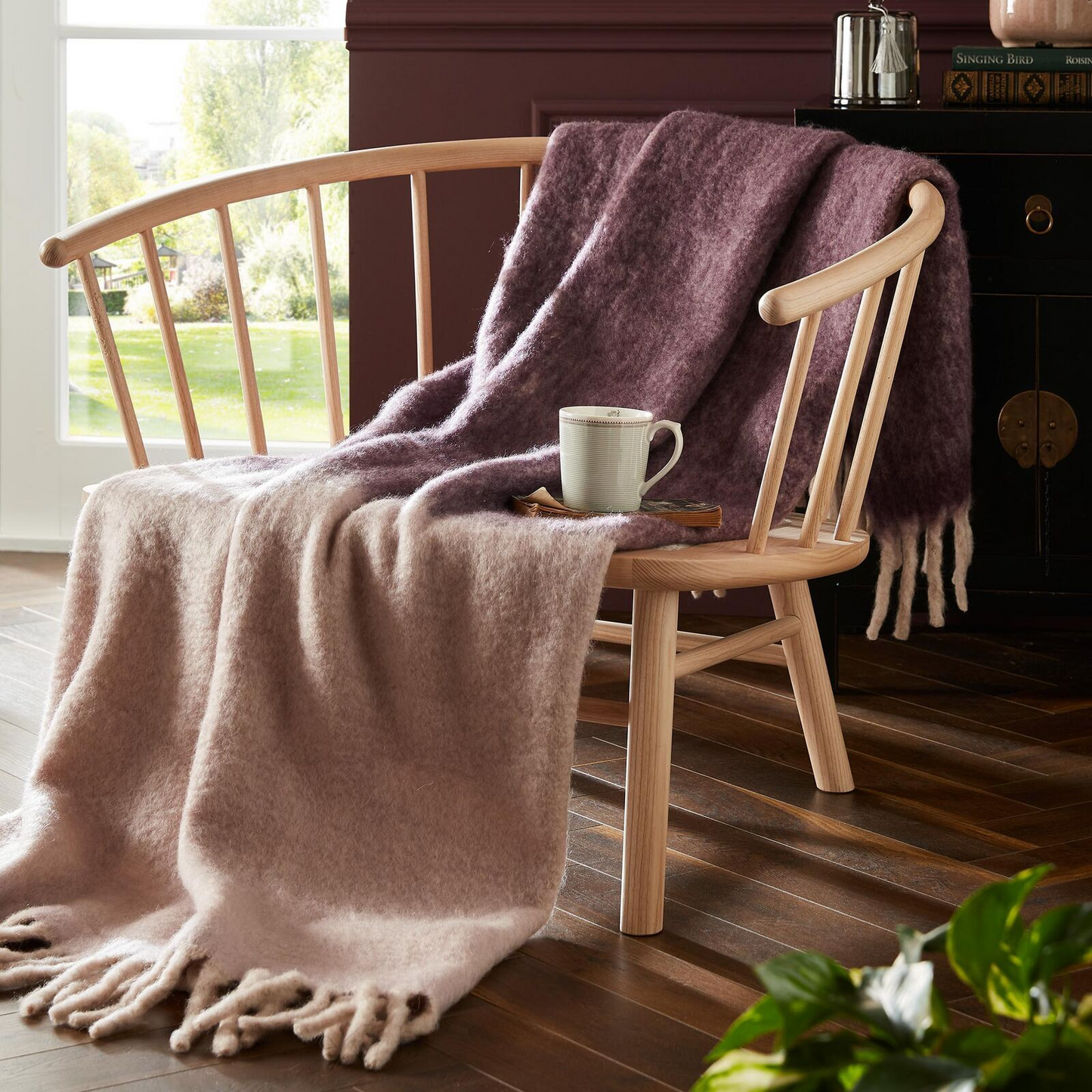 Wooden chair with draped blankets and a cup of coffee in a cozy room.