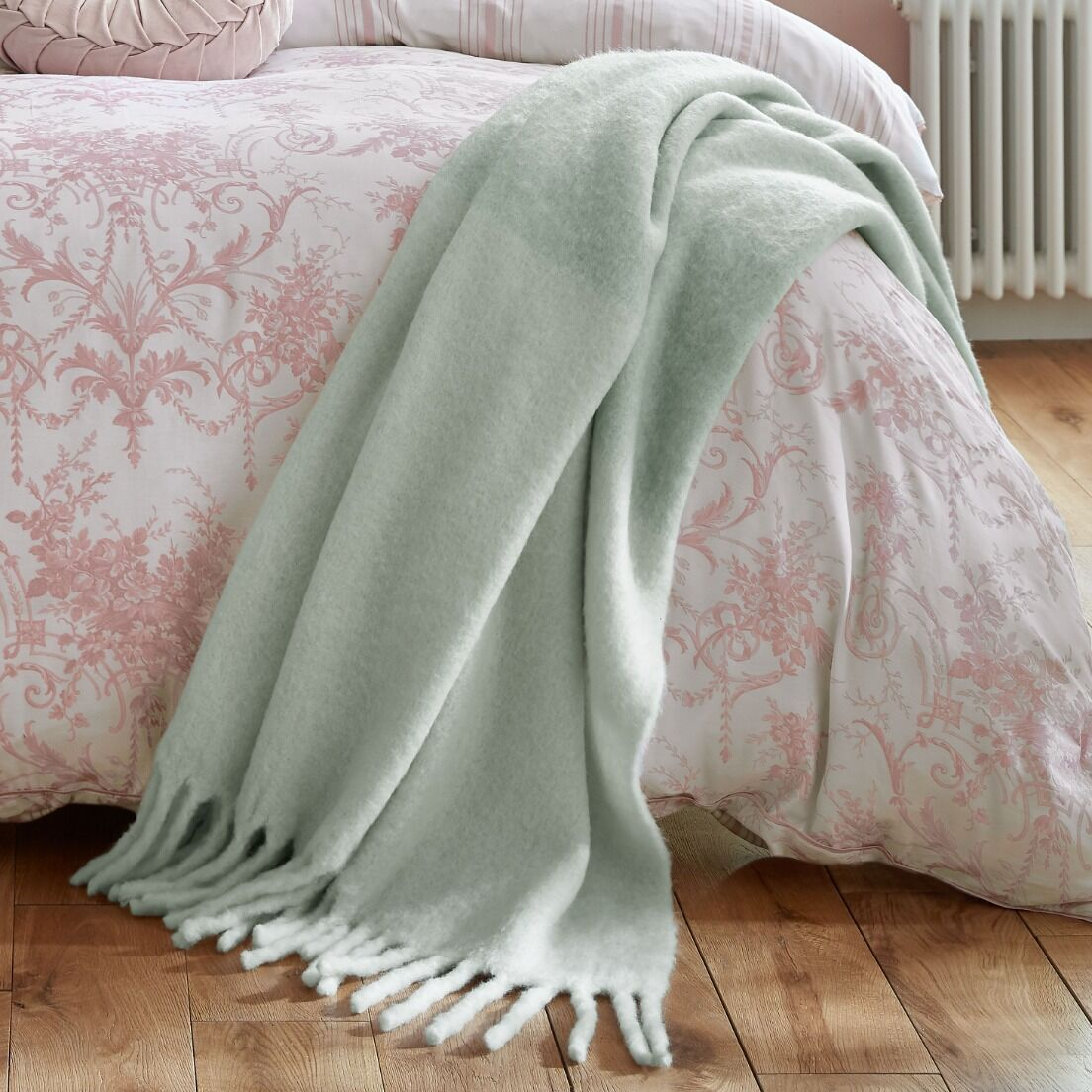 Light green throw blanket on a bed with pink floral bedding