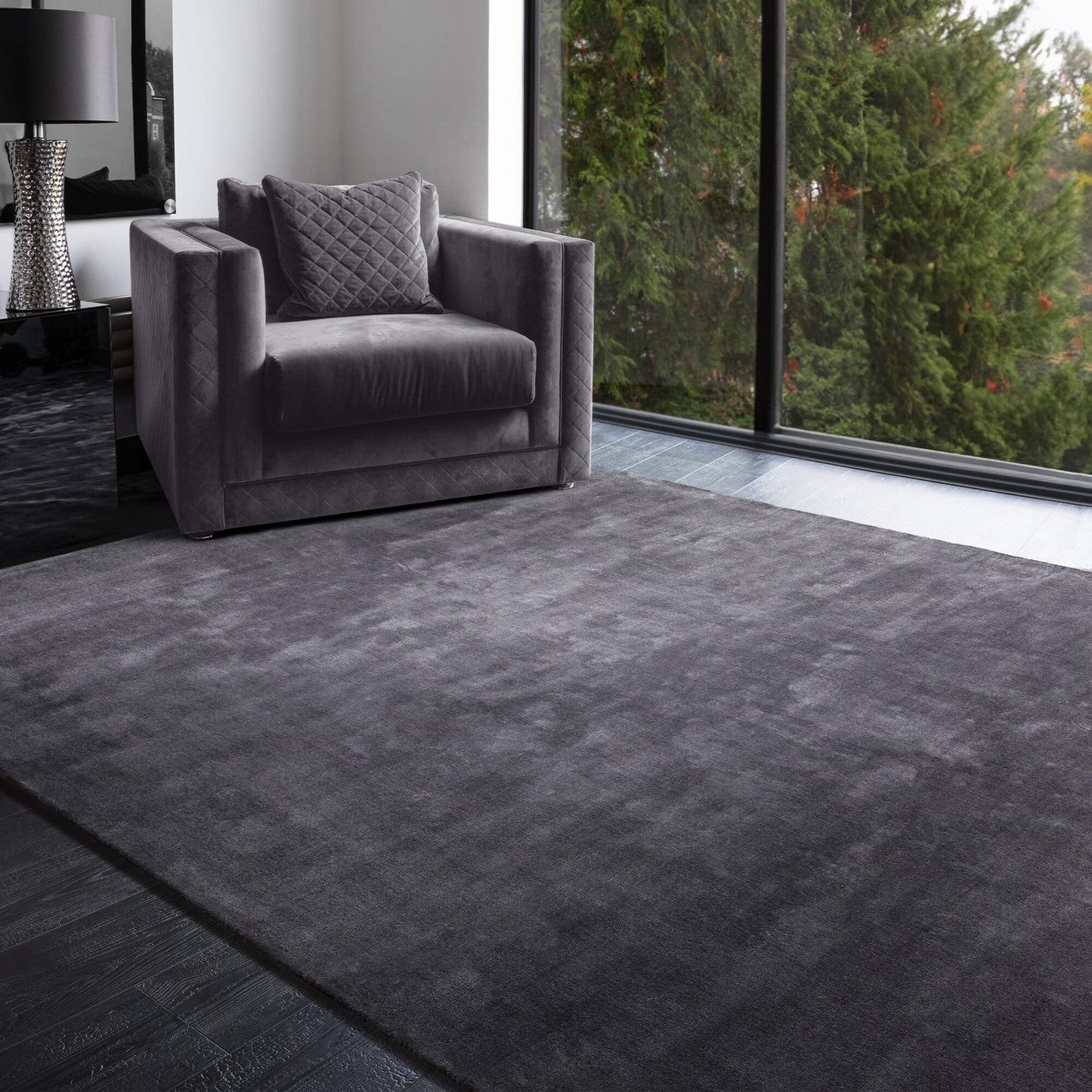 Gray armchair on a textured gray rug in a modern living room with large windows.
