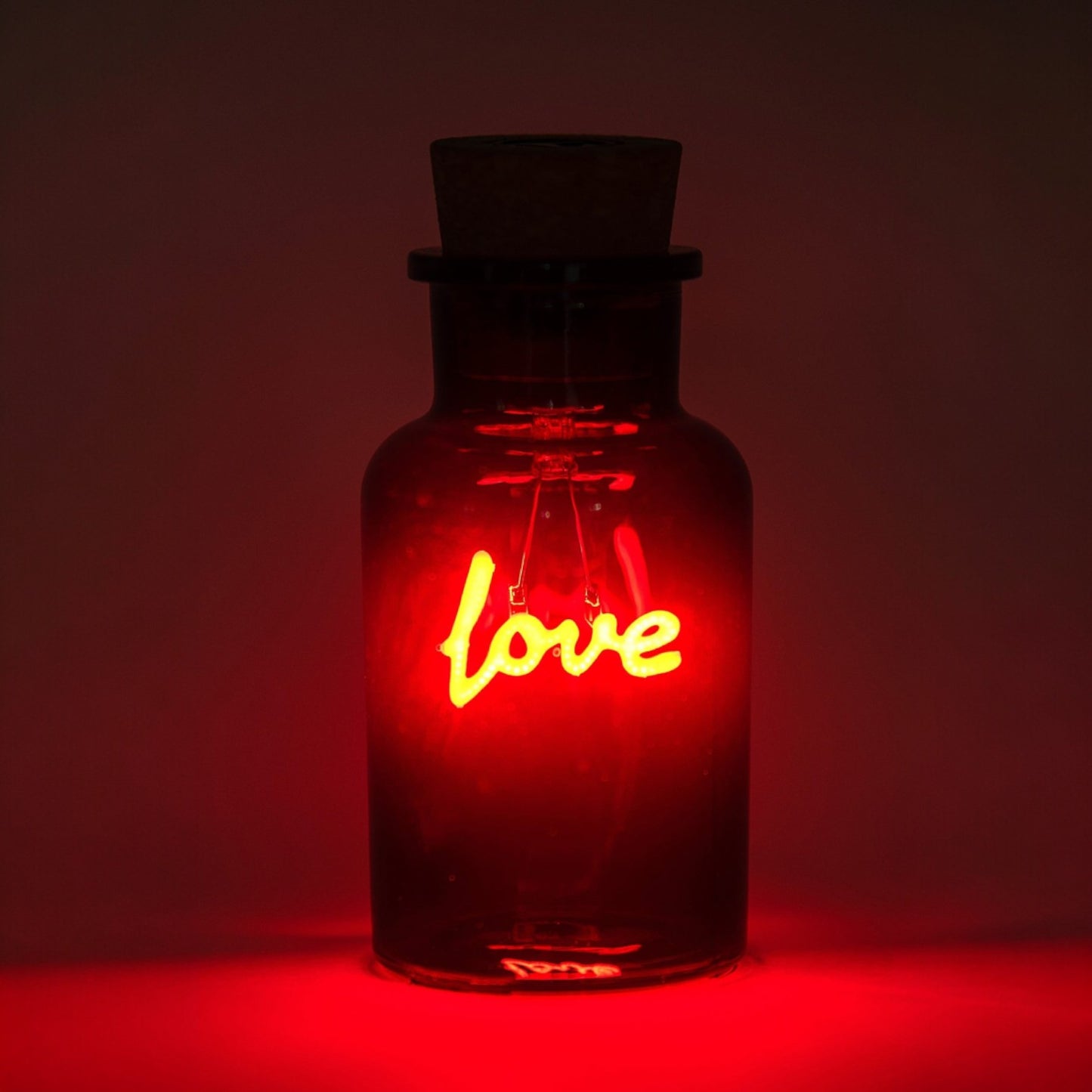 Neon sign that says 'love' inside a red-lit glass bottle against a dark background