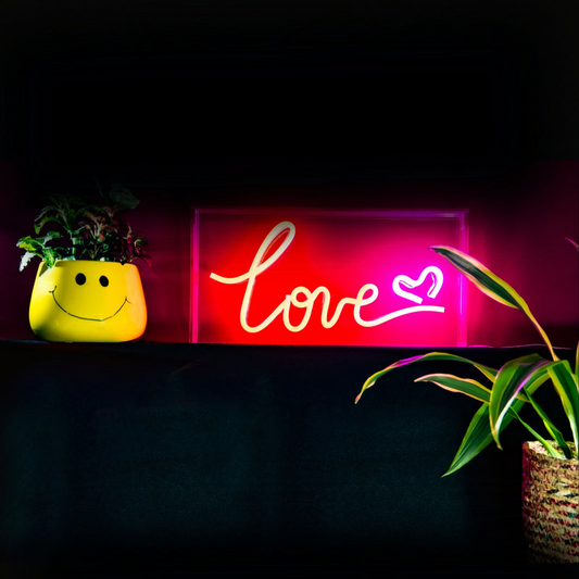 Neon sign with 'love' text on a dark background with plants