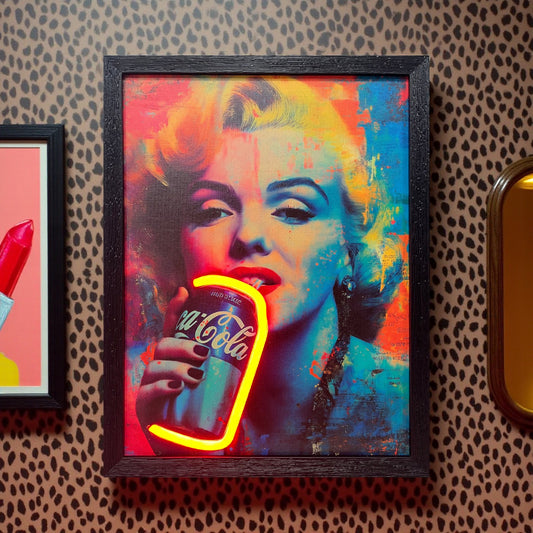 Framed artwork of a colorful depiction of Marilyn Monroe holding a Coca-Cola bottle on a patterned wall.