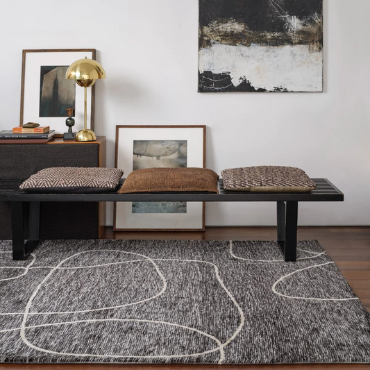 Modern interior with a black bench, textured cushions, and abstract art on a gray rug.