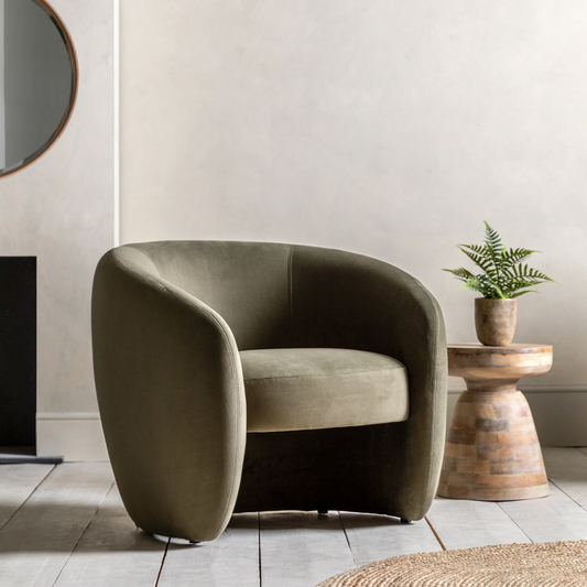 Modern olive green armchair in a room with a wooden side table and plant.