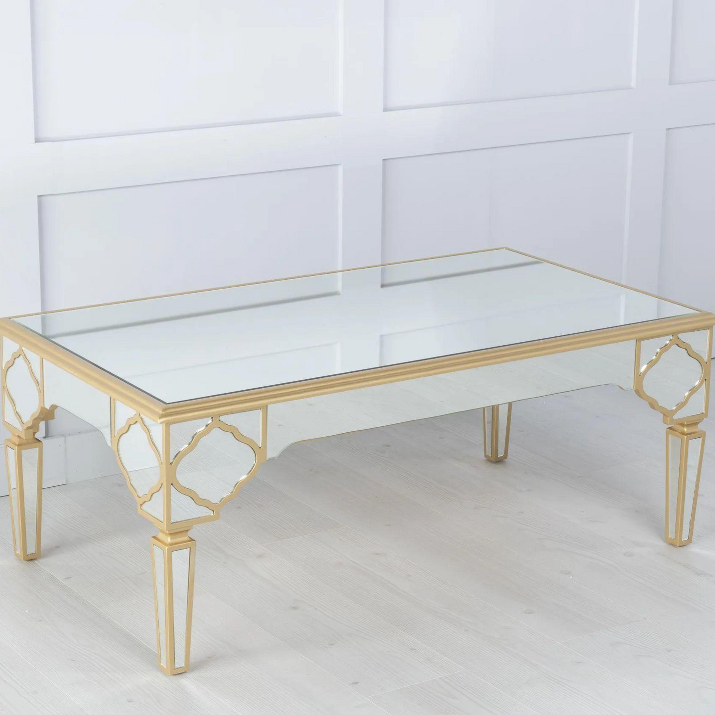 Gold-framed glass coffee table against a white paneled wall.