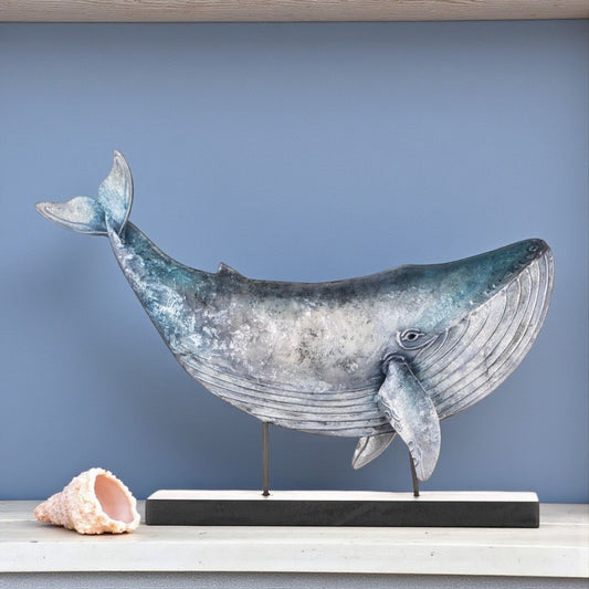 Whale sculpture on a stand with a shell beside it against a blue background