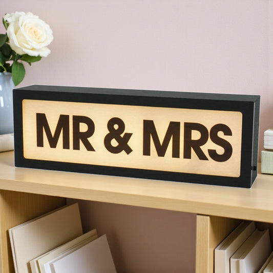 Decorative sign with 'MR & MRS' on a shelf with flowers in the background