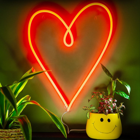 Neon heart light with a yellow smiley face pot and plants on a dark background