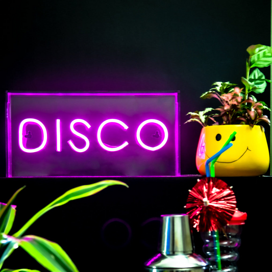 Neon 'DISCO' sign with a cocktail shaker and plants on a dark background